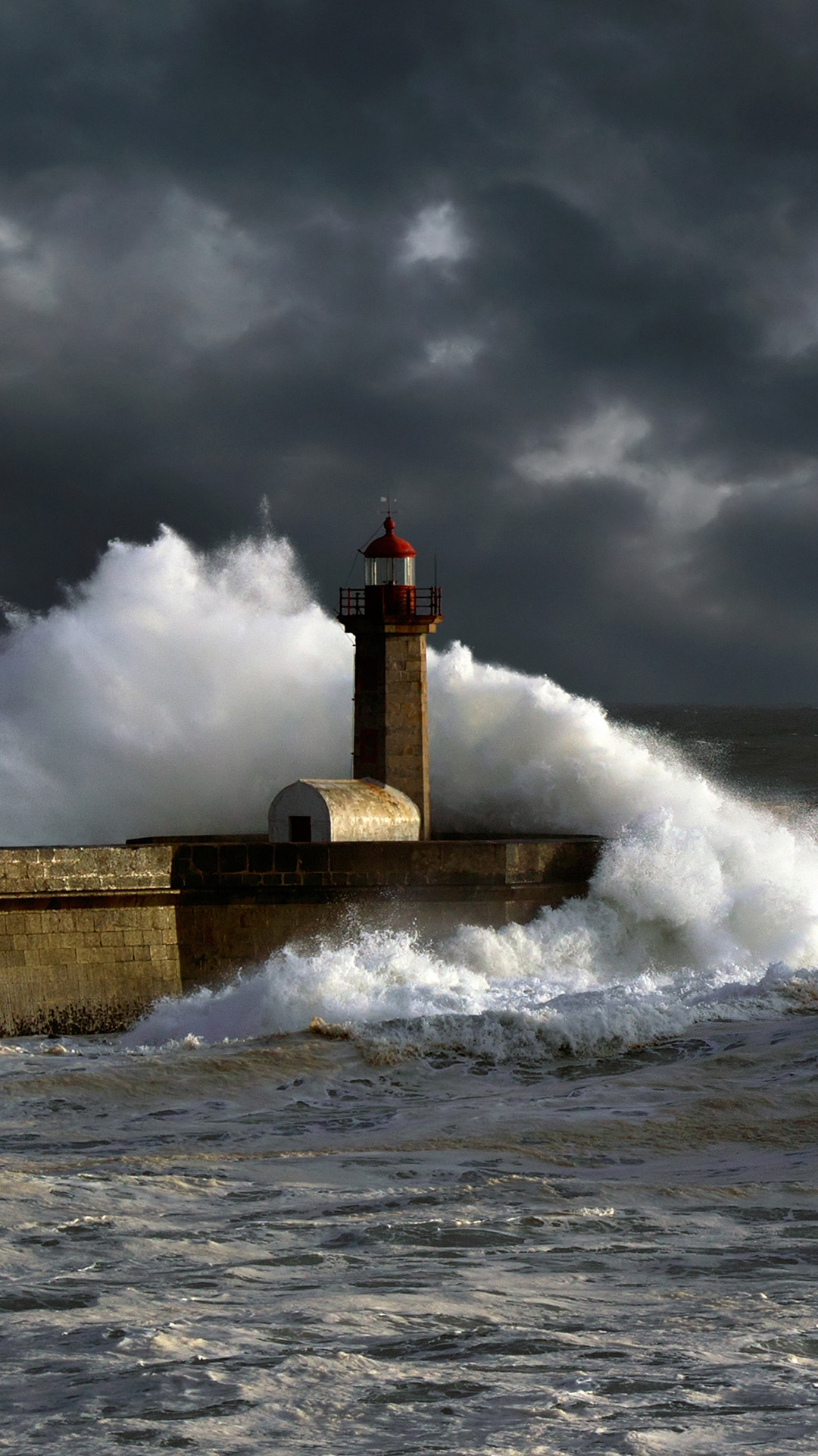 Stormy sunset at the harbor of the mouth of the river Douro, in Porto, Portugal, with big waves against old lightouse, new pier and beacon; enhanced sky